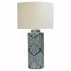 The Marco Polo table lamp has a cylindrical blue ceramic base with a white floral pattern and is topped with a large, round white lampshade.