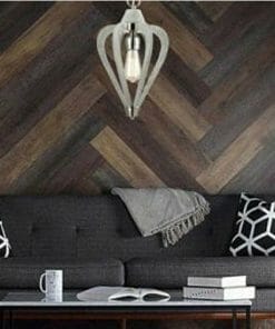 A modern living room showcases the Senorita Series: a dark gray sofa with geometric pillows, a cozy gray throw, and a wooden coffee table holding books and a mug, set before a herringbone wood wall under a chic pendant light.