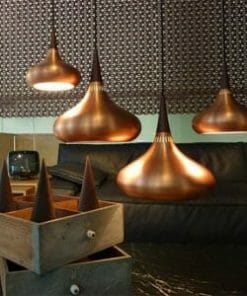 Four Nona pendant lights with copper teardrop designs hang above a dark sofa, while wooden boxes holding conical objects sit on the table in front.