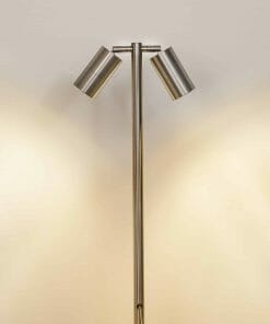 The Tivah HV1405-SS316 is a metal floor lamp with two cylindrical shades angled apart, casting light on a plain wall—ideal for achieving a Spike Spotlight effect in any modern space.