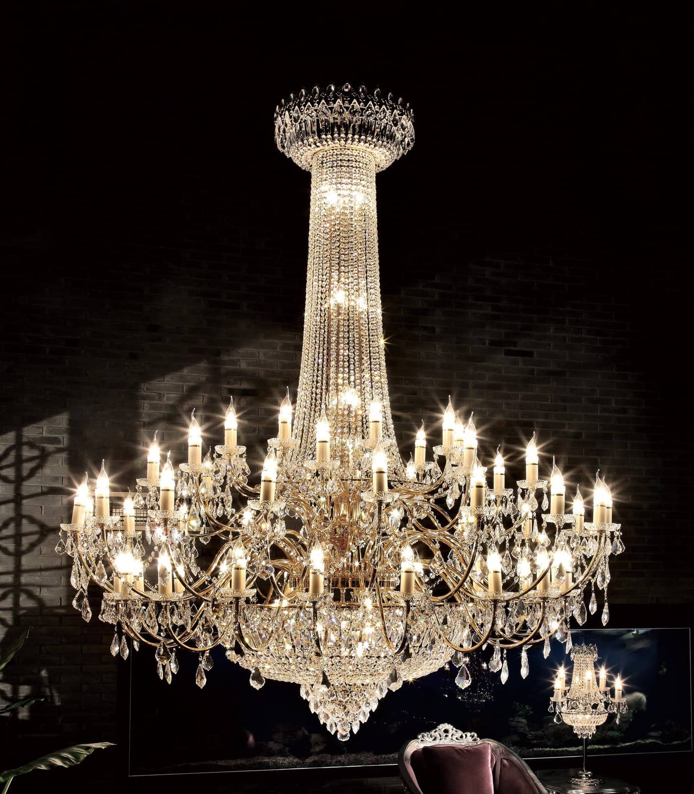 The Asfour crystal 6000 - 47" 51 Light chandelier features multiple tiers and 51 candle-style lights, glowing against a dark background with a chair partially visible below.