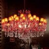 An Asfour crystal 6631-71" 42 light pendant with red crystal ornaments and multiple lit lampshades is suspended from the ceiling in a dimly lit room.