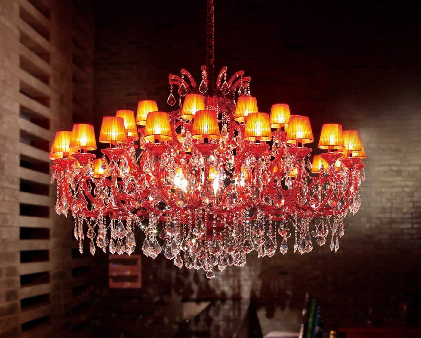 An Asfour crystal 6631-71" 42 light pendant with red crystal ornaments and multiple lit lampshades is suspended from the ceiling in a dimly lit room.