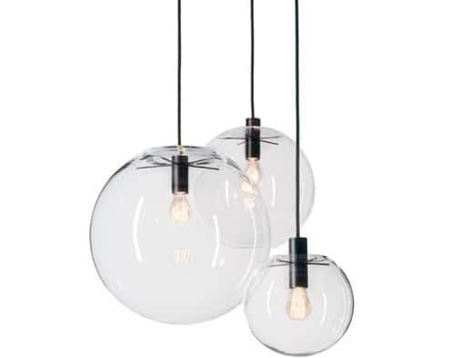 Three Linder Selene Replica Clear Pendant lights with glass globes and black cords hang at different heights, each featuring a visible bulb for a modern look.