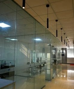 Modern office interior featuring the VIVA Pendant in Matt Black, with glass-walled conference rooms, ceiling lights, and a shiny tile floor. Empty chairs and desks are visible through the glass partitions.