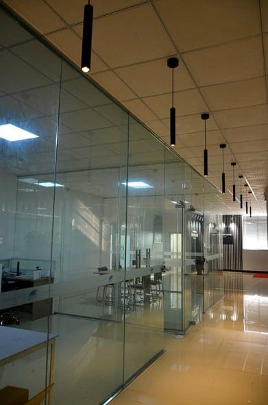 Modern office interior featuring the VIVA Pendant in Matt Black, with glass-walled conference rooms, ceiling lights, and a shiny tile floor. Empty chairs and desks are visible through the glass partitions.