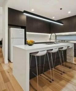 Modern kitchen with dark cabinets, white countertops, a large island and wood flooring. A Gamma 80W black or white LED light brightens the space, highlighting the refrigerator and built-in appliances.