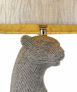 The Nala table lamp showcases a bejeweled panther or leopard head base and is topped with a light lampshade featuring gold trim.