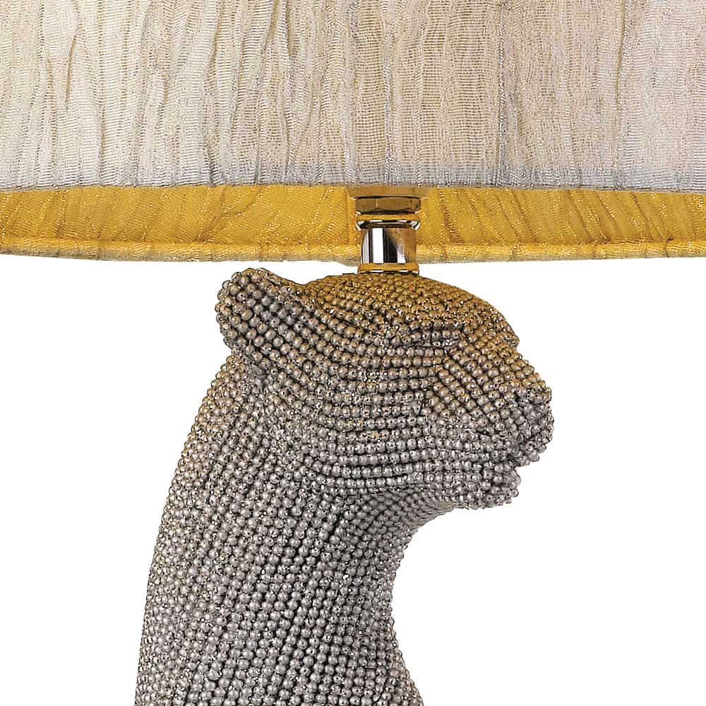 The Nala table lamp showcases a bejeweled panther or leopard head base and is topped with a light lampshade featuring gold trim.