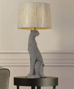 The Nala table lamp has a gray textured dog-shaped base and a round beige fabric shade, adding charm to any black circular side table.