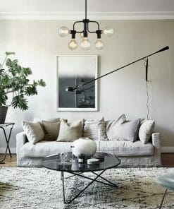 A modern living room featuring a white sofa, neutral cushions, round glass coffee table, indoor plant, wall art, and the Hexa 6 light pendant as a statement ceiling fixture.