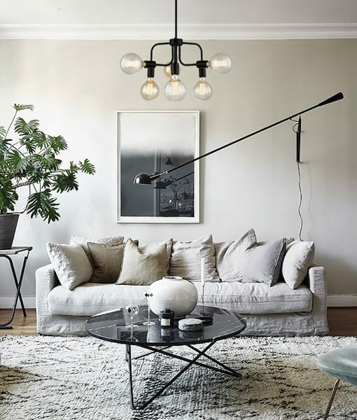 A modern living room featuring a white sofa, neutral cushions, round glass coffee table, indoor plant, wall art, and the Hexa 6 light pendant as a statement ceiling fixture.