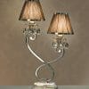 The Luxuria 2 light table lamp has a silver curved base, two brown pleated shades, and crystal accents, all set against a beige patterned background.