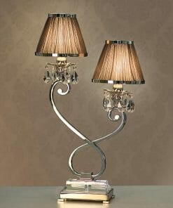 The Luxuria 2 light table lamp has a silver curved base, two brown pleated shades, and crystal accents, all set against a beige patterned background.