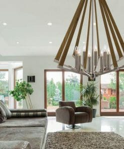 A modern living room features large windows, a sectional sofa, two armchairs, a rug, potted plants, and is illuminated by the Graf 8 timber pendant. Natural light streams into the space.