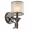 The Lacey wall light is a wall-mounted bronze sconce with a cylindrical frosted glass shade that emits soft, warm light.