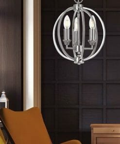 A Kendall 3 light chrome/black chandelier with exposed bulbs hangs in a room with dark paneled walls, a yellow chair, and white decorative lanterns.