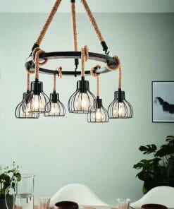 The Rampside 6 black metal chandelier with rope accents and six exposed bulbs hangs above a dining table set for two, while plants and wall art provide a stylish background.