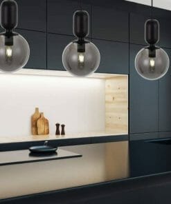 Modern kitchen featuring Kade 1 Smoke cabinets, built-in cooktop, minimalist sink, three globe pendant lights, wooden cutting boards, and a light wood accent shelf.