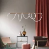 Modern interior featuring the swife linear abstract pendant light, pink curtains, minimalist chairs, and a small shelf with decorative items set against a neutral wall.