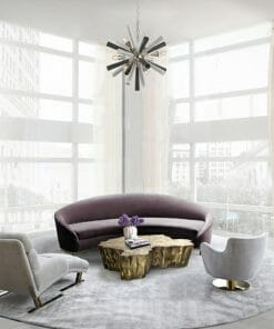 Modern living room featuring a curved purple sofa, two gray chairs, a gold geometric coffee table, the Spunik 6 chandelier, and large windows with sheer curtains.