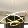 The Tuscan 3 Ring Black chandelier showcases interlocking black and gold rings suspended by wires, creating a modern statement against a neutral interior backdrop.