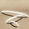 Three modern Tuscan 3 ring black LED pendant lights of different sizes hang in a spiral from the ceiling against a neutral background.