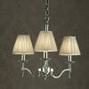 The Standford 12 Chrome Shimmer Grey chandelier features three lights with pleated beige lampshades and a polished metal frame, hanging by a chain against a textured dark background.
