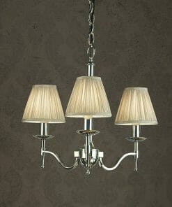 The Standford 12 Chrome Shimmer Grey chandelier features three lights with pleated beige lampshades and a polished metal frame, hanging by a chain against a textured dark background.