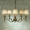 A Standford 3 Antique brass Shimmer shade chandelier with six arms hangs from the ceiling against patterned wallpaper.