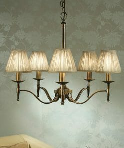 A Standford 3 Antique brass Shimmer shade chandelier with six arms hangs from the ceiling against patterned wallpaper.