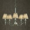 The Standford 12 Chrome Shimmer grey chandelier features five lights with pleated fabric shades, elegantly suspended by a chain against a textured dark wall.