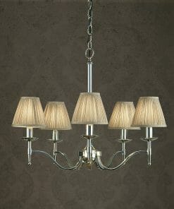 The Standford 12 Chrome Shimmer grey chandelier features five lights with pleated fabric shades, elegantly suspended by a chain against a textured dark wall.