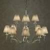 The Standford 12 Chrome Shimmer grey chandelier, featuring twelve arms and pleated beige shades, adds elegant sparkle against a textured grey wall.