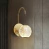 The Langton 1 black wall sconce showcases a round, textured glass shade that glows elegantly against a textured brown wall.