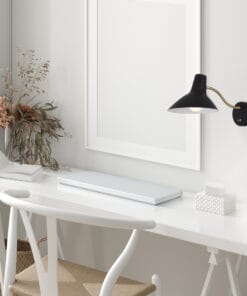 Minimalist white desk setup featuring a chair, open book, closed laptop, dried flowers in a vase, and the sleek Farbon Short Wall Light mounted on a light-colored wall.