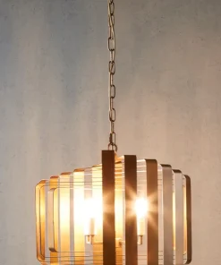 The Brontel 4 brass pendant light features layered rectangular metal and glass panels, suspended by a chain from the ceiling, casting a warm glow against a neutral wall.